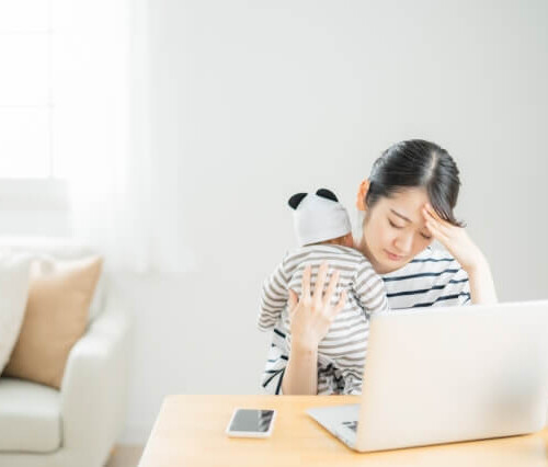 赤ちゃんを抱っこしながらパソコンの前で悩む女性