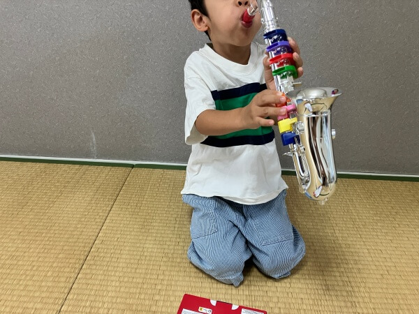５歳の男の子がサックスのおもちゃを練習しています。