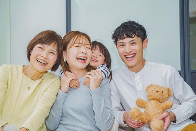 楽しそうに笑う、おばあちゃんとおかあさんに抱き着いている女の子、くまのぬいぐるみを持ったお父さん